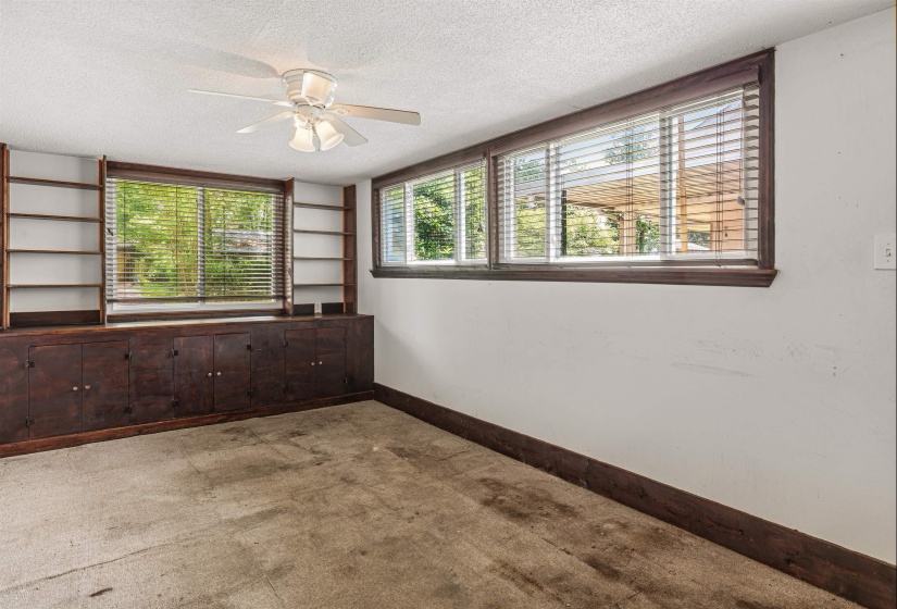 Room featuring built-in cabinetry and shelving, multiple windows with dark wood trim, and a ceiling fan
