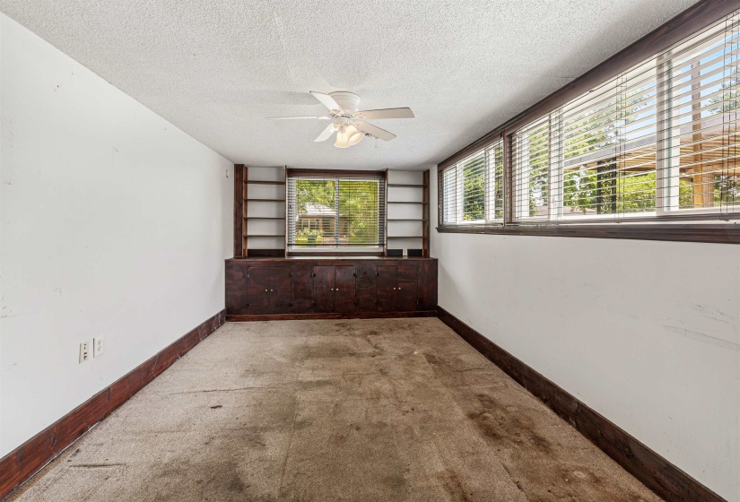 Room featuring built-in dark wood cabinetry with shelving, a ceiling fan, and multiple windows with blinds