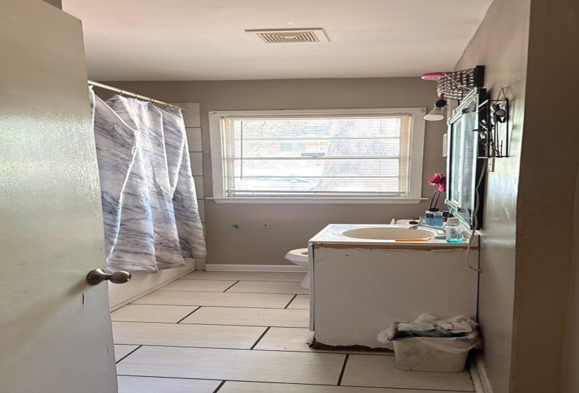 Bathroom featuring a window with blinds, a vanity with an integrated sink, a toilet, and light-colored tile flooring