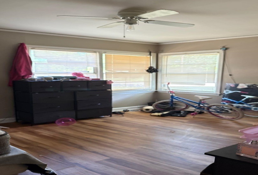 Bright room featuring wood-finish flooring, a ceiling fan with integrated lighting, and multiple windows with blinds