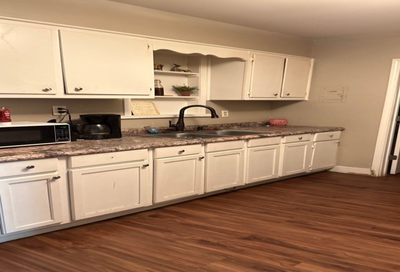 Kitchen featuring wood-finish flooring, white cabinetry, a double basin sink with a dark-finish faucet, and a patterned countertop