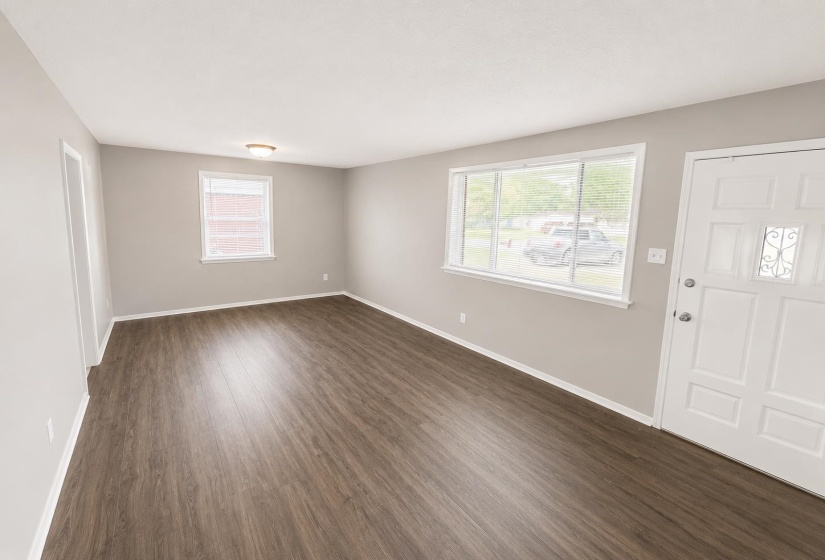 Spacious room featuring wood-finish flooring, light grey painted walls, white baseboards, and a white paneled entry door with decorative glass inserts