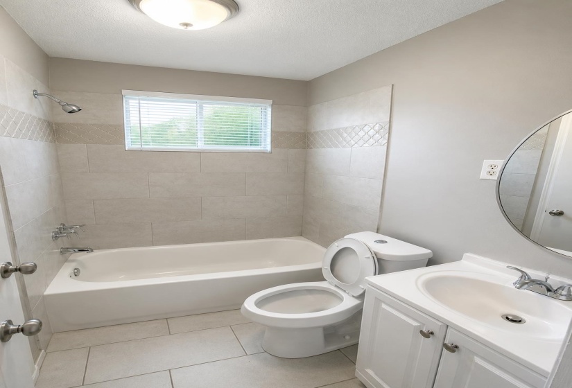 Full bathroom featuring a white tub, shower with light-toned tile surround, and decorative accent banding