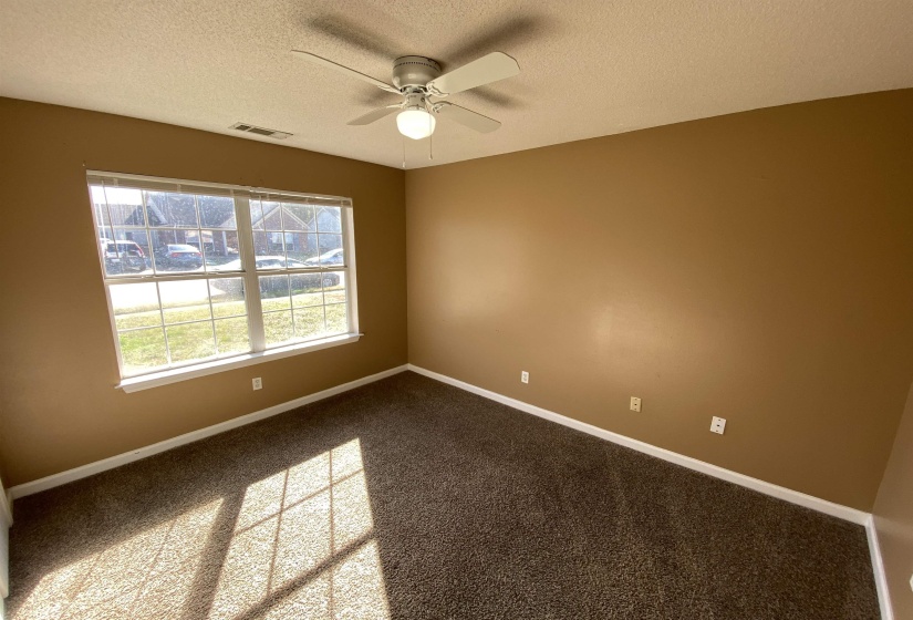 Carpeted room featuring a large window, a ceiling fan with integrated lighting, and neutral-toned wall paint