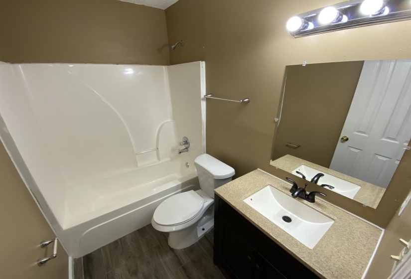 Full bathroom featuring a white tub/shower combination, dark wood-finish vanity with an integrated sink, light-toned countertop, and wood-finish flooring