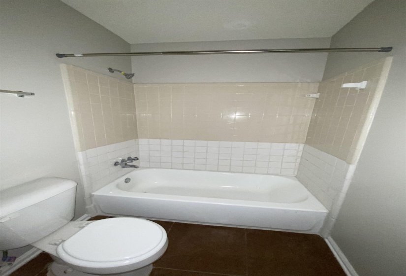 Bathroom featuring a white bathtub, two-tone wall tiling, chrome shower fixtures, and a white toilet