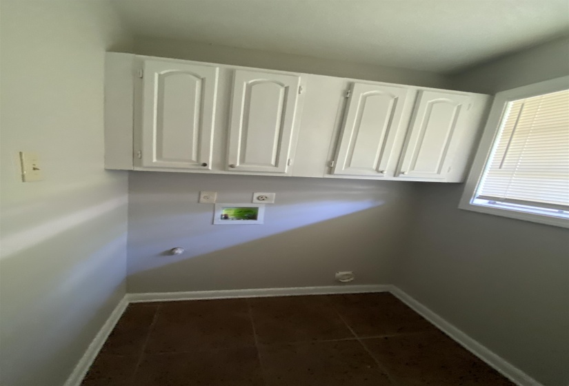 Utility room featuring upper cabinetry, tile flooring, and a window with blinds