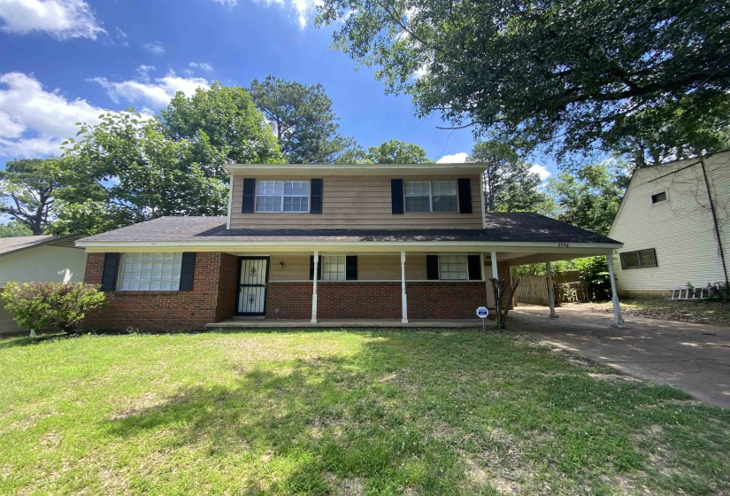 Two-story residence featuring brick and siding facade, covered front porch, attached carport, and mature trees