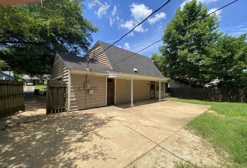 Exterior featuring a covered patio, concrete paving, wood fencing, and mature trees