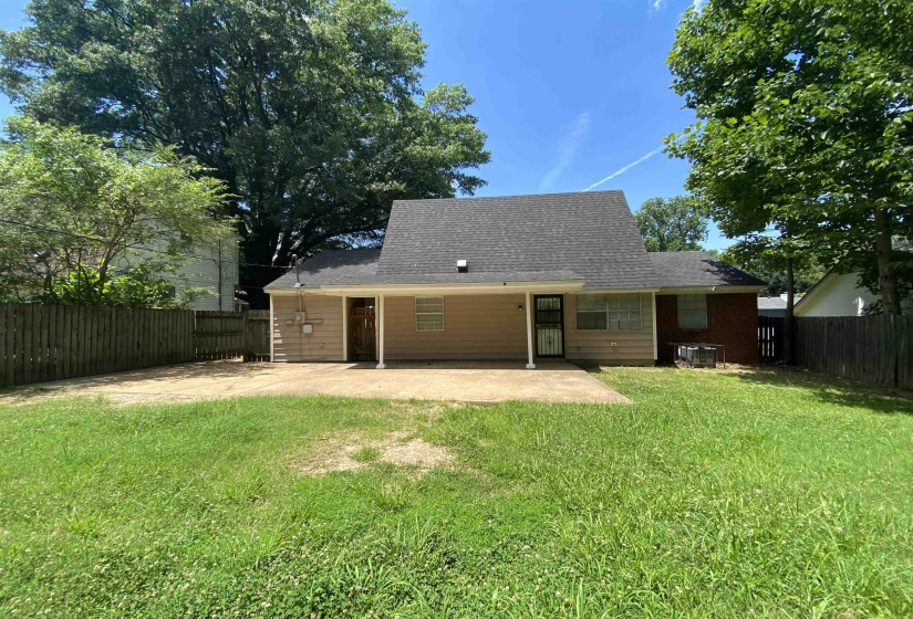 Expansive rear yard featuring a concrete patio, wood privacy fencing, and mature trees