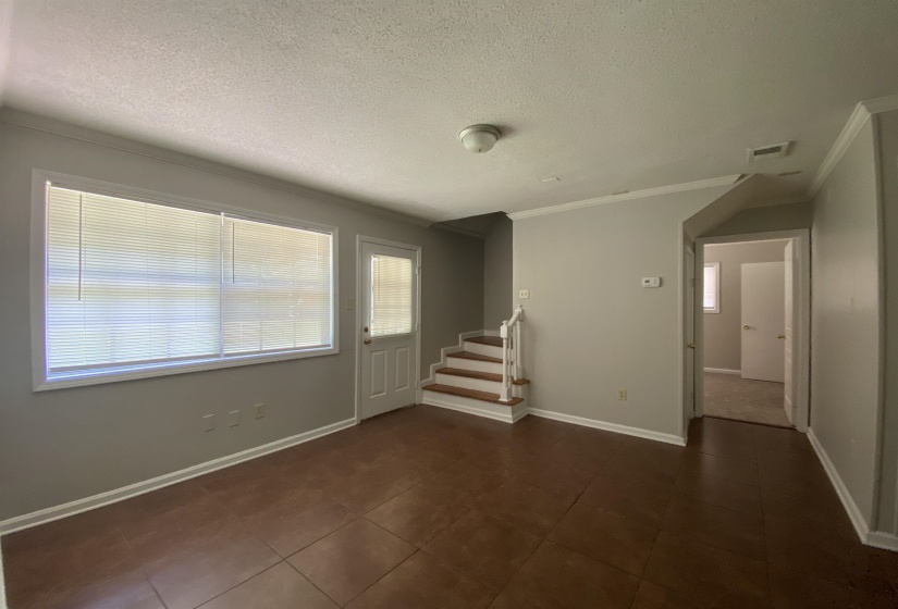Interior space featuring tile flooring, a large window with blinds, a white paneled door with a glass insert, and a staircase with wood-finish treads and white risers