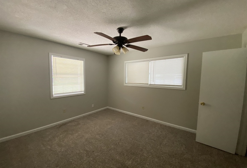 Spacious room featuring neutral carpeting, light-toned wall paint, and two windows with white blinds