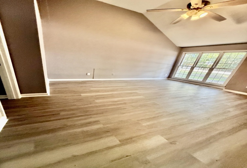 Vaulted ceiling great room featuring wood-finish flooring, a ceiling fan fixture, and multiple large windows with muntins