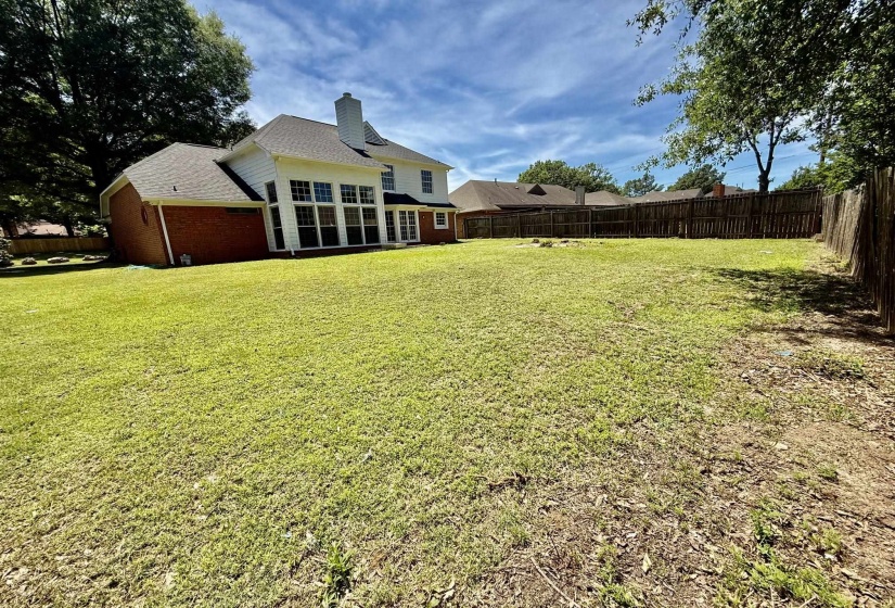 Expansive backyard featuring a large green space, partial privacy fencing, and mature perimeter trees