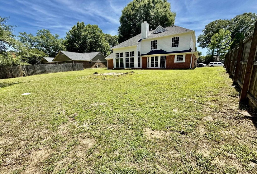 Expansive rear yard featuring a large green space, a two-story white siding and brick exterior, numerous windows, and a privacy fence