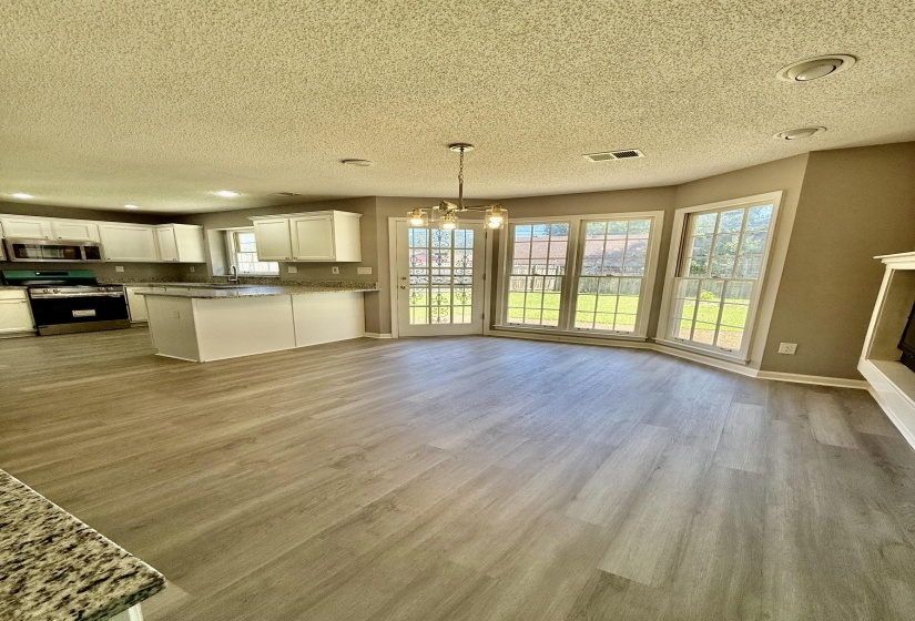 Open-concept kitchen and dining area featuring light wood-finish flooring, a kitchen island with stone-finish countertops, white cabinetry, a chandelier, and multiple paneled windows