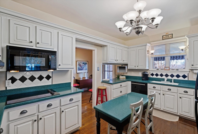 Kitchen featuring white cabinetry, teal countertops, black and white diamond-patterned tile backsplash, and a built-in cooktop and microwave