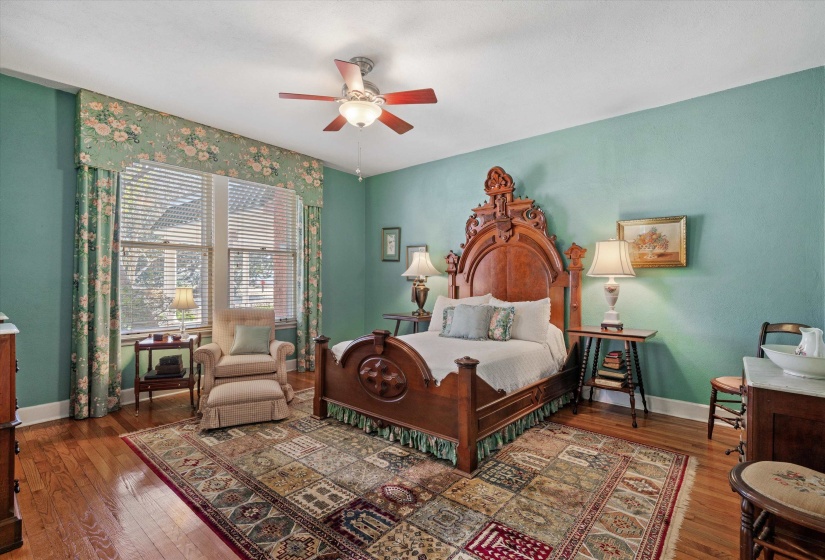 Spacious room featuring wood-finish flooring, a ceiling fan with integrated lighting, and multiple windows with blinds and patterned valances