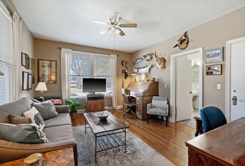 Spacious living area featuring warm wood-finish flooring, a ceiling fan fixture, and multiple windows providing natural light