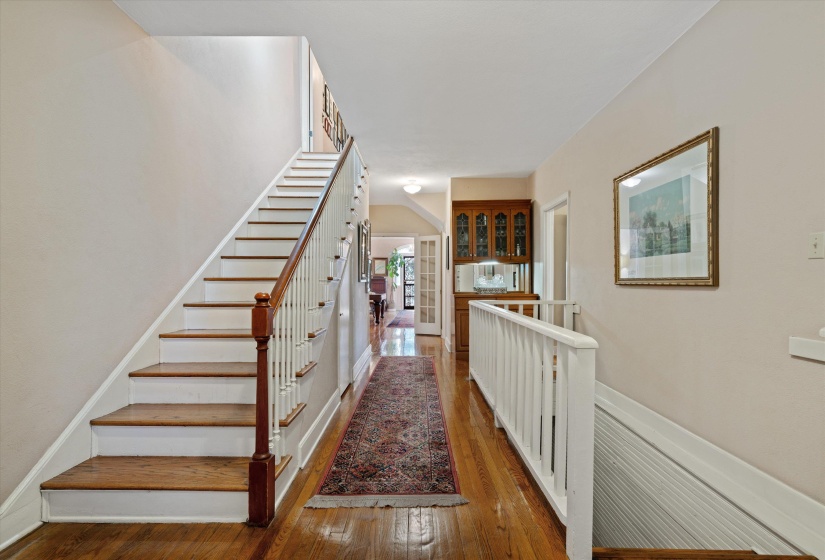 Hardwood flooring extending through a central hallway featuring a staircase with white risers, wood treads, and a white balustrade with a wood newel post