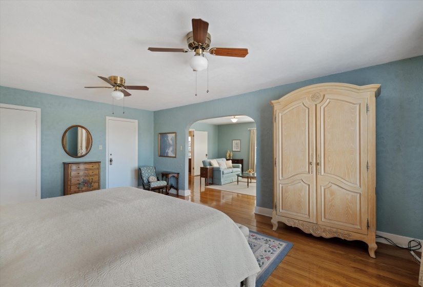 Hardwood flooring extending into an arched doorway, two ceiling fans, and a light blue wall finish