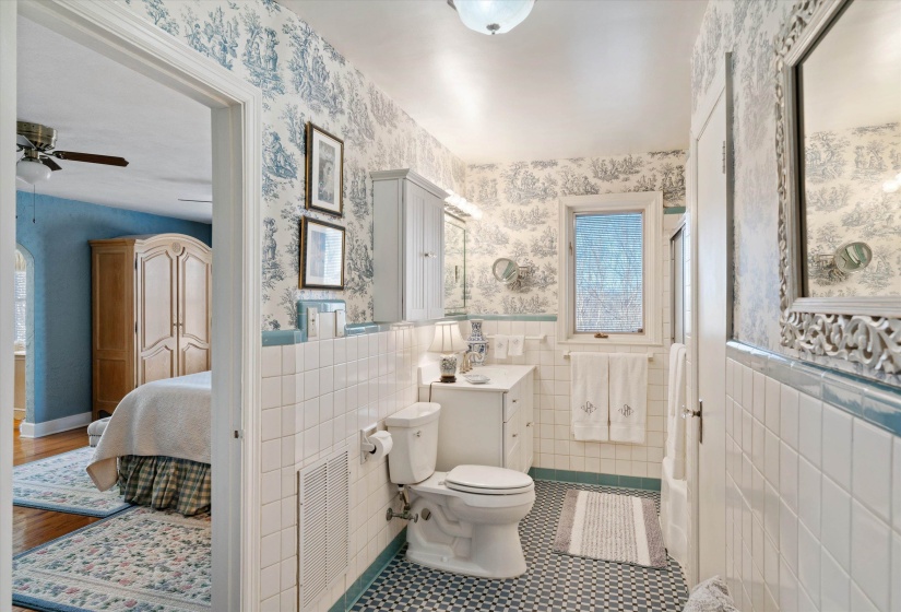 Bathroom featuring white tile walls with a blue trim, patterned wallpaper, and a window providing natural light