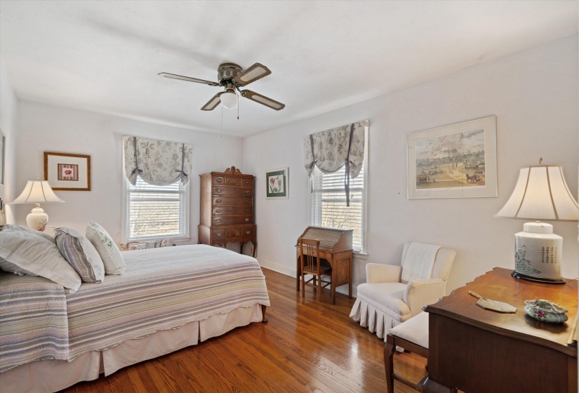 Bright room featuring wood-finish flooring, two windows with blinds and fabric valances, a ceiling fan with integrated lighting, and white walls