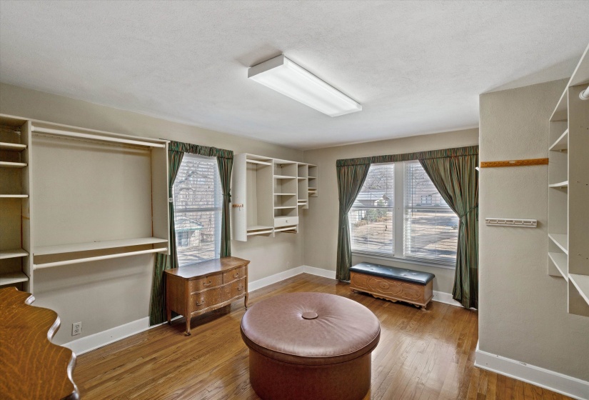 Expansive dressing room featuring wood-finish flooring, built-in shelving, hanging rods, and two windows