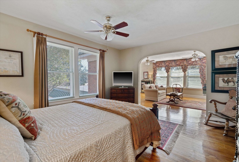 Bedroom featuring wood-finish flooring, a ceiling fan with light fixture, and a large window with tan drapery