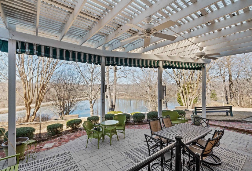 Expansive stone paver patio featuring a white pergola with two integrated ceiling fans and striped retractable awnings