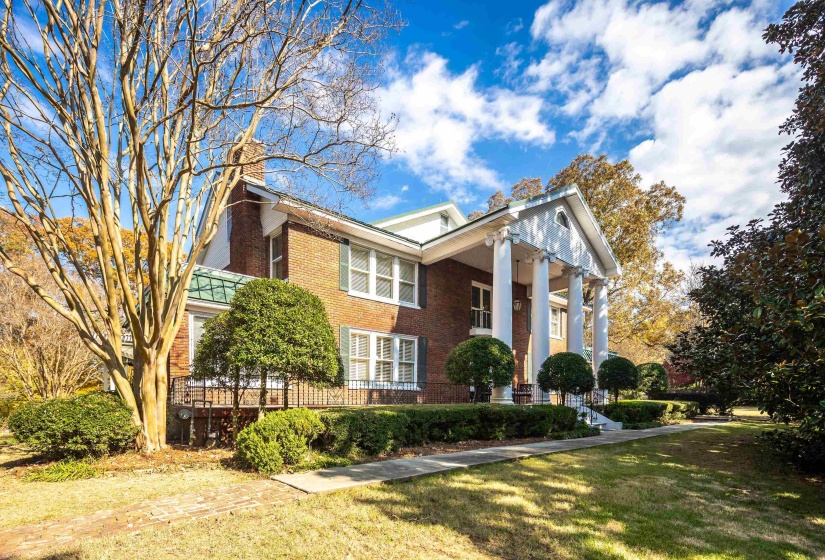 Brick exterior featuring a portico with classical columns, a traditional front walkway, mature landscaping, and a green metal roof accent