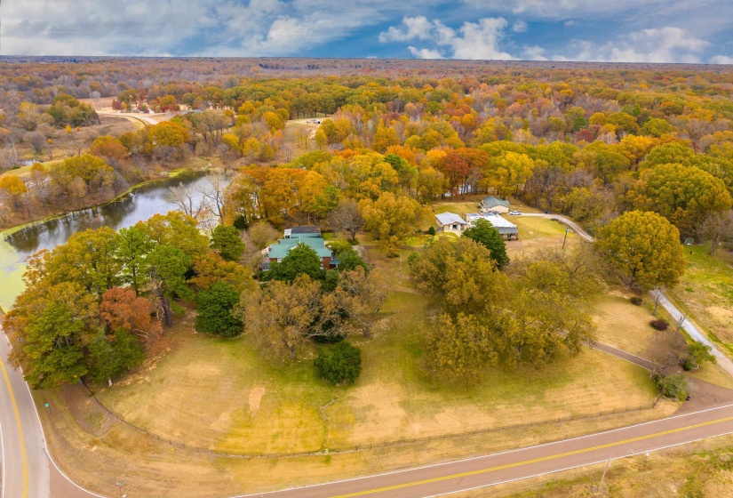 Expansive property featuring a pond, established trees, and multiple structures