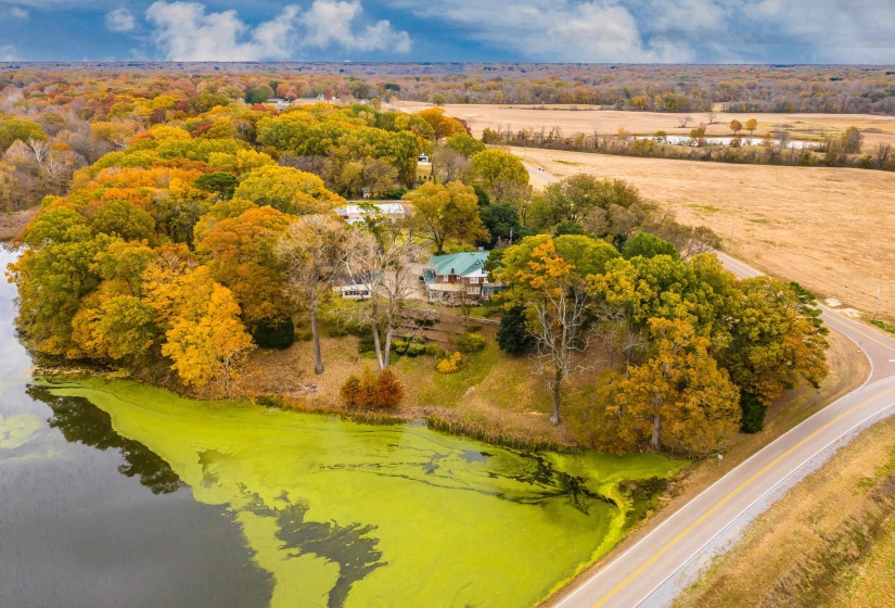 Expansive property featuring a curved paved road, mature trees with autumn foliage, and a water body