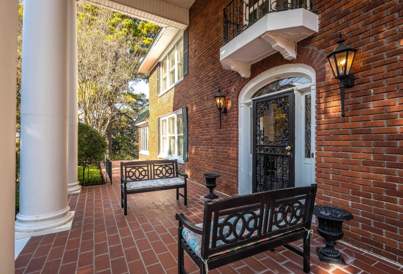 Brick exterior featuring a covered porch, decorative black iron door, arched entryway, and white columns