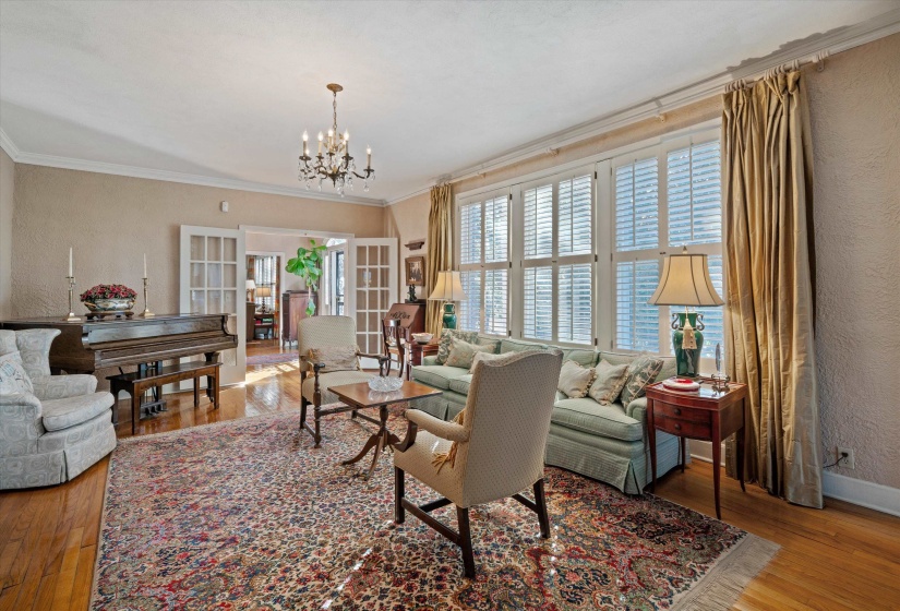 Spacious room featuring hardwood flooring, multiple windows with white plantation shutters, and a classic chandelier light fixture