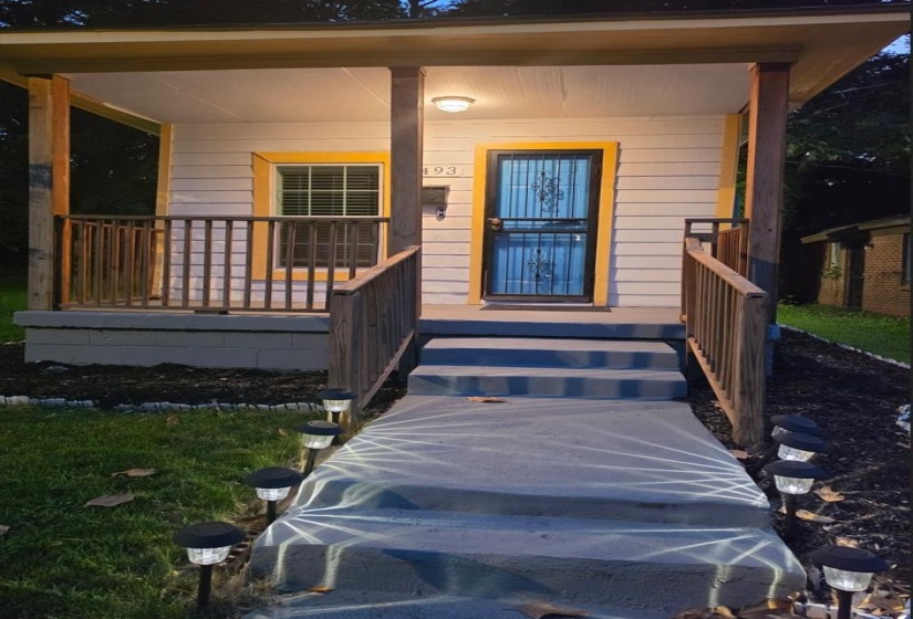 Front exterior featuring light-colored siding, a covered porch with natural wood railings, and a multi-step concrete entryway