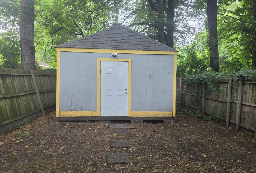 Detached shed with light blue siding and yellow trim, featuring a white door