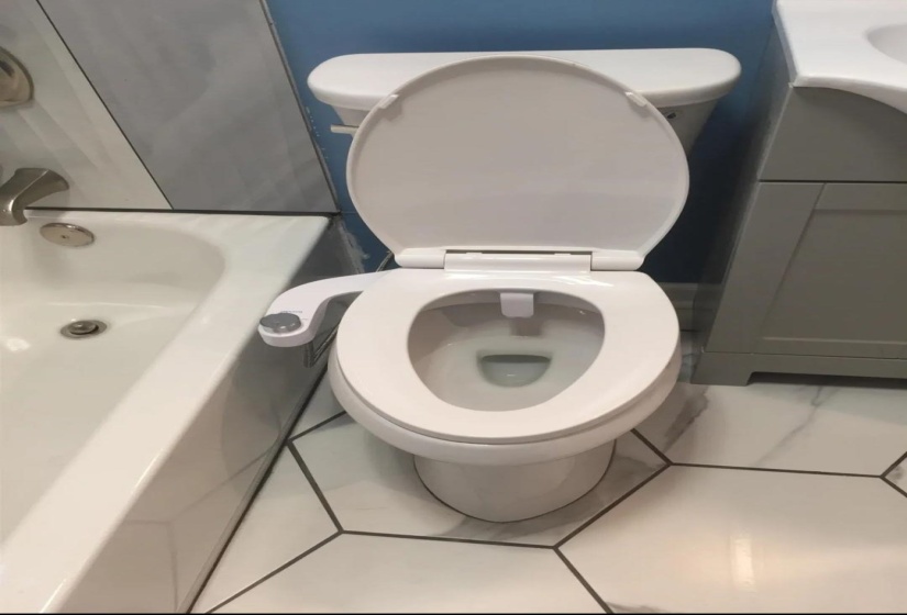 White toilet with bidet attachment, hexagonal floor tiling, and a white soaking tub