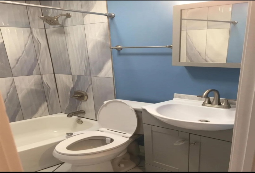 Full bathroom featuring a white bathtub, tiled shower surround with a brushed nickel showerhead, single vanity with a white basin, and a mirrored medicine cabinet