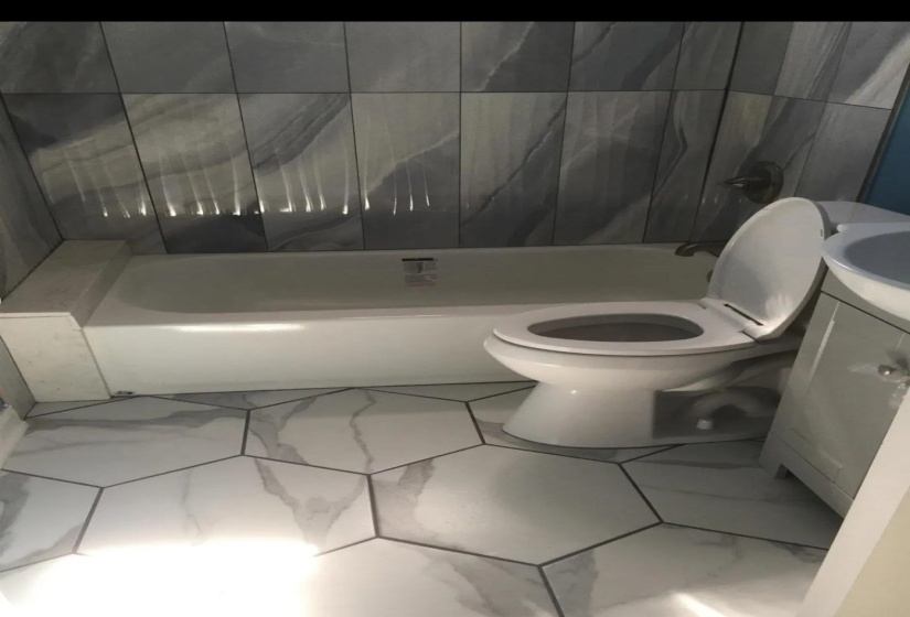 Bathroom featuring a white bathtub, a toilet, a white vanity with a basin sink, and hexagonal floor tiles