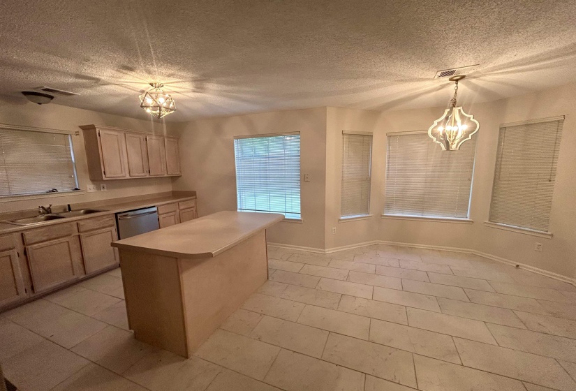 Kitchen featuring a central island, light wood-finish cabinetry, stainless steel dishwasher, and tile flooring