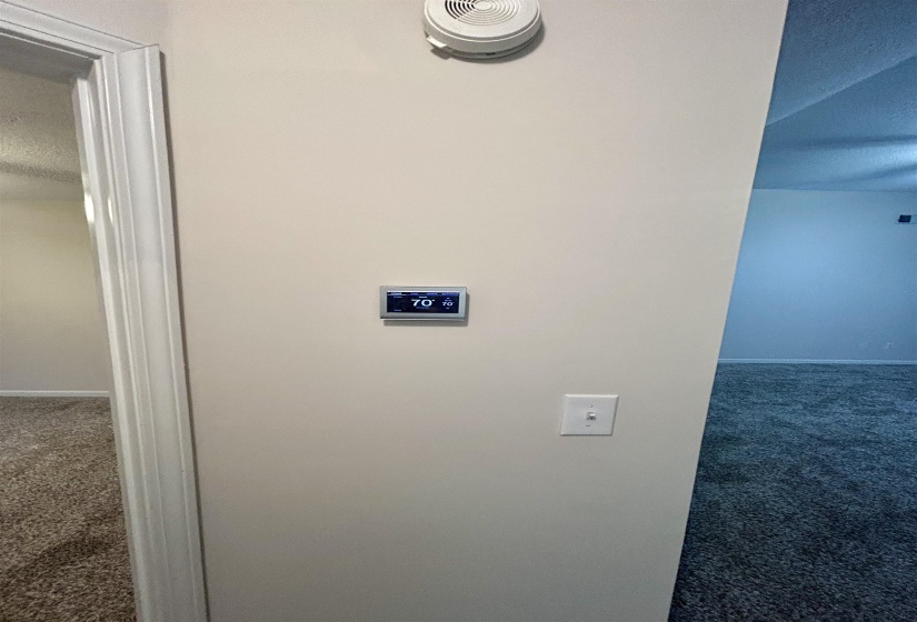 Digital thermostat control, light-colored wall with white trim, and a smoke detector