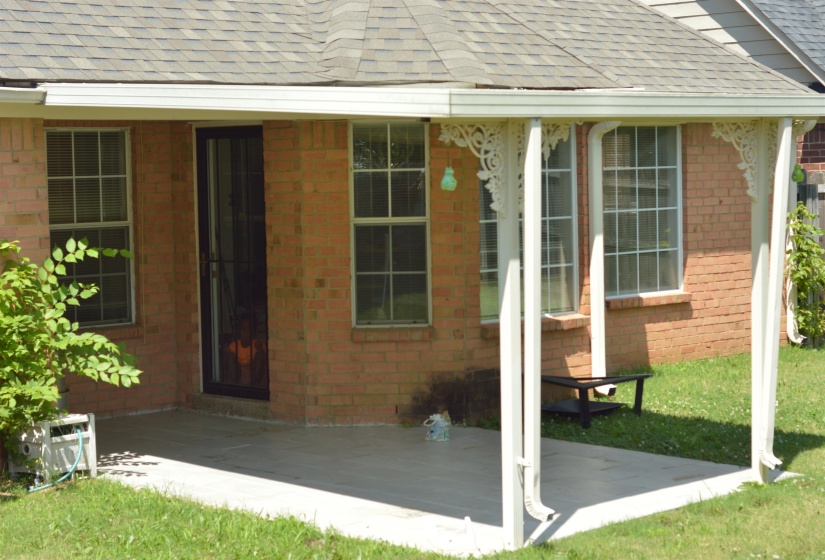 View of exterior entry with roof with shingles, a patio area, brick siding, and a yard