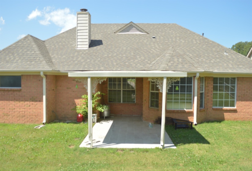 Back of property featuring a patio area, brick siding, a chimney, and a shingled roof