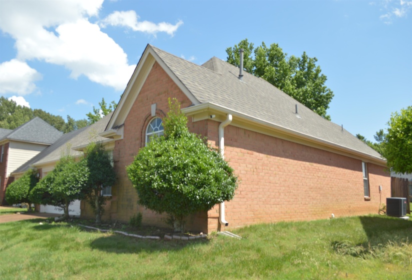 View of side of home with brick siding, cooling unit, and a lawn