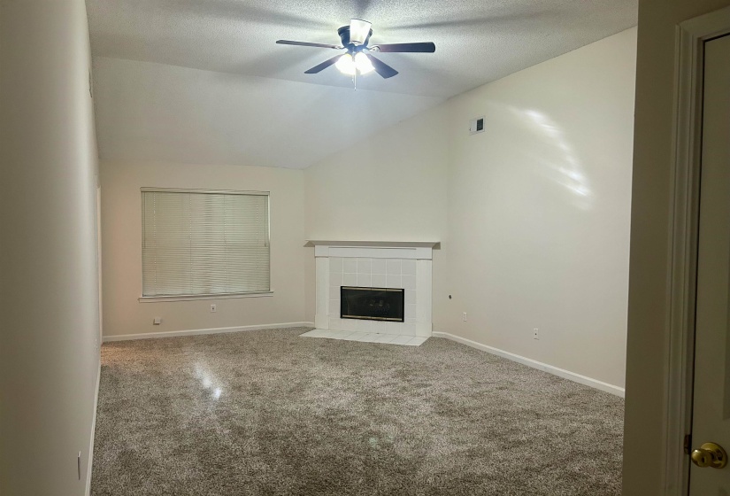 Vaulted ceiling living space featuring a white tile fireplace with a black firebox, a single window with blinds, and recessed lighting
