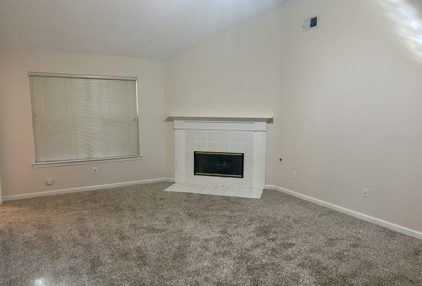 Living room featuring a fireplace with white tile surround, a mantel, vaulted ceiling, and carpeted flooring