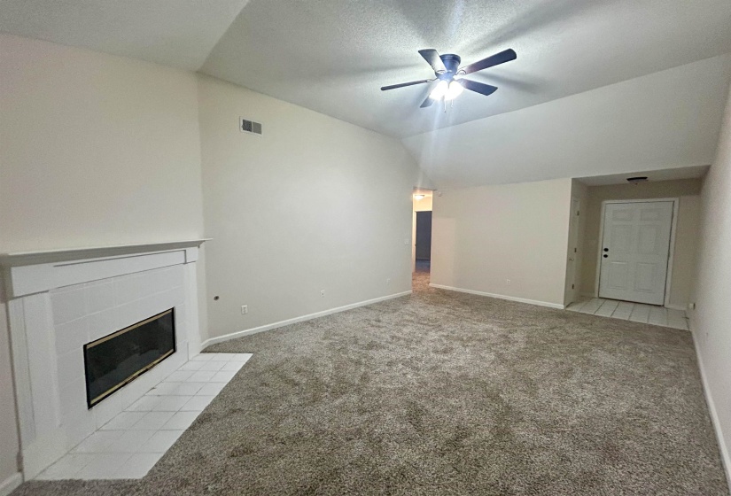 Spacious living area featuring vaulted ceilings, a ceiling fan, plush carpeting, and a fireplace with a white mantel and tile hearth