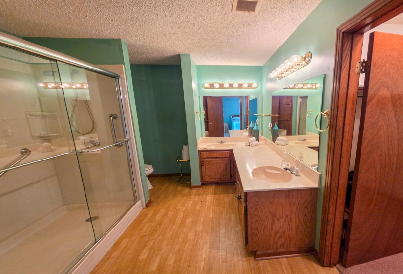 Bathroom featuring a glass-enclosed shower, dual vanity with integrated sinks, wood-finish flooring, and a vanity-width mirror with overhead lighting