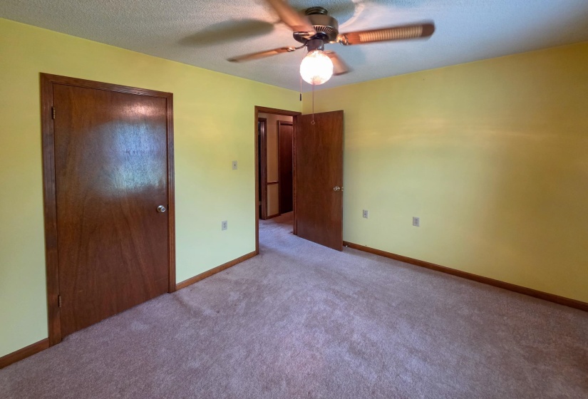 Carpeted interior room featuring a ceiling fan with light fixture, wood-finish doors, and baseboard trim